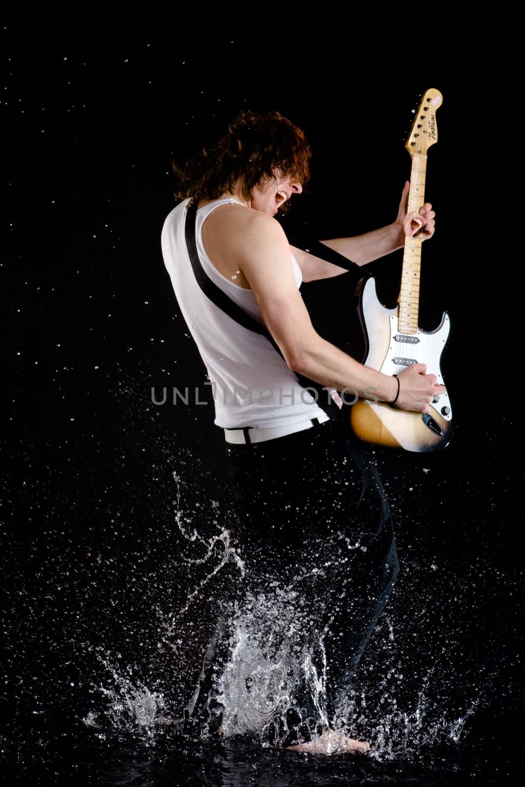 Portrait of young performer playing electrical guitar in water splashes and singing