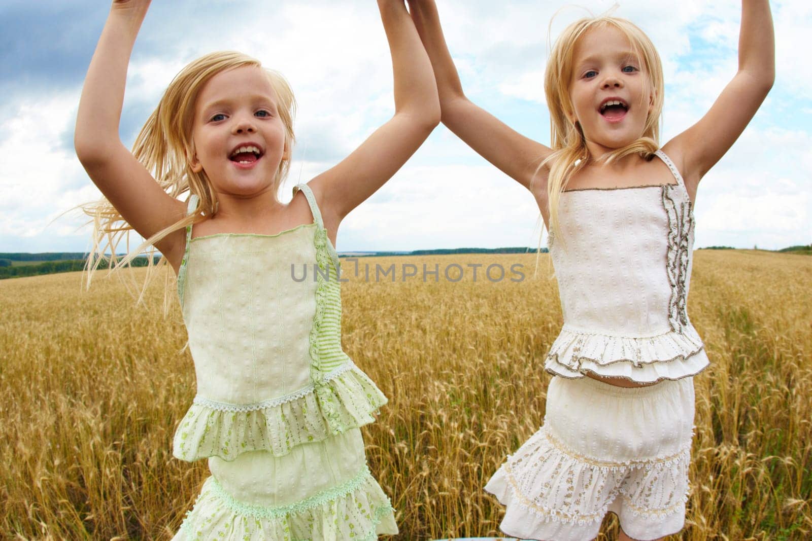 Portrait of energetic twin sisters jumping in wheat field and having fun