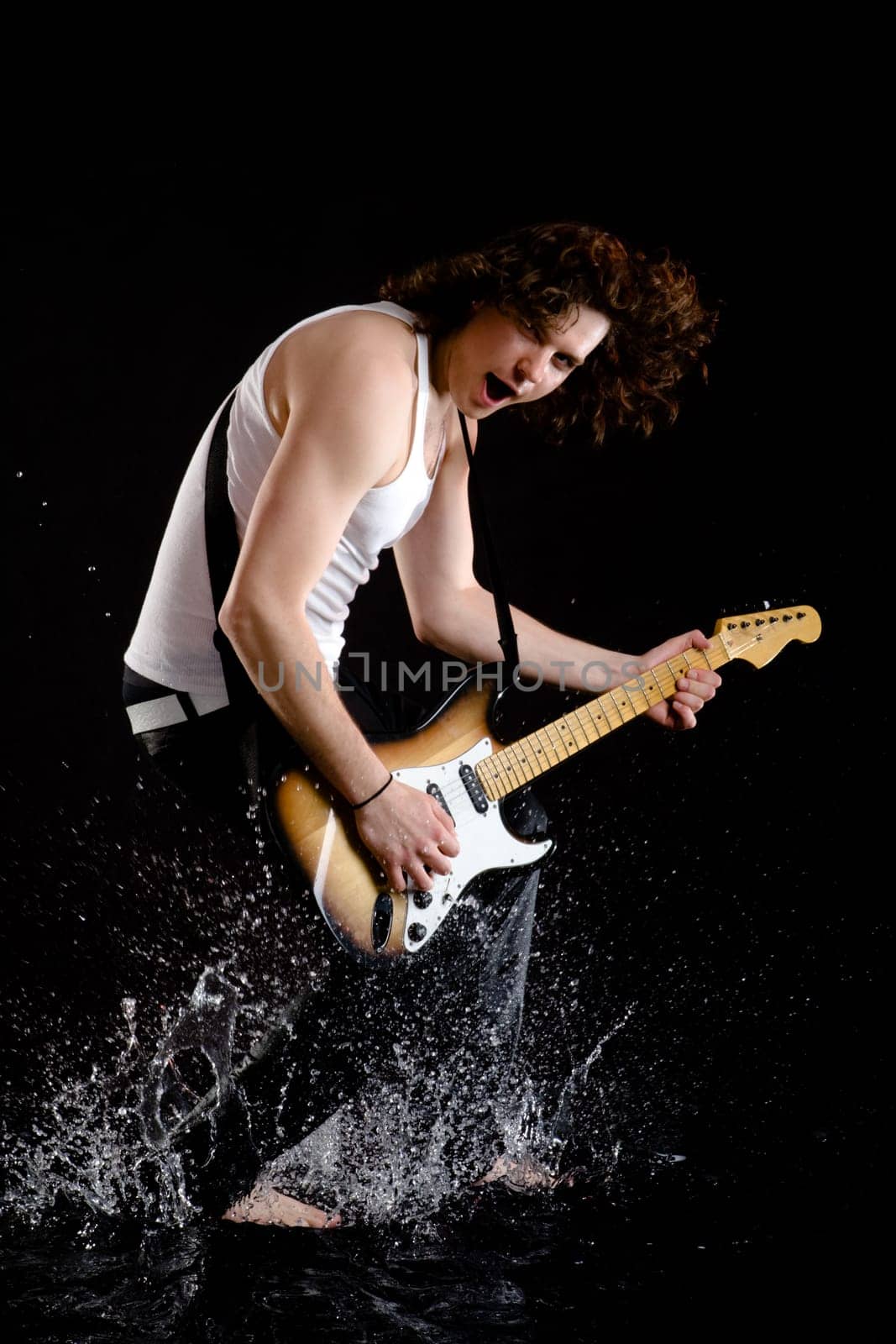 Portrait of young guitarist playing instrument while walking in water and singing
