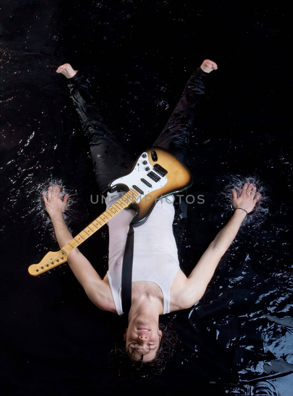 Above shot of happy guitarist in vest lying in water and looking at camera