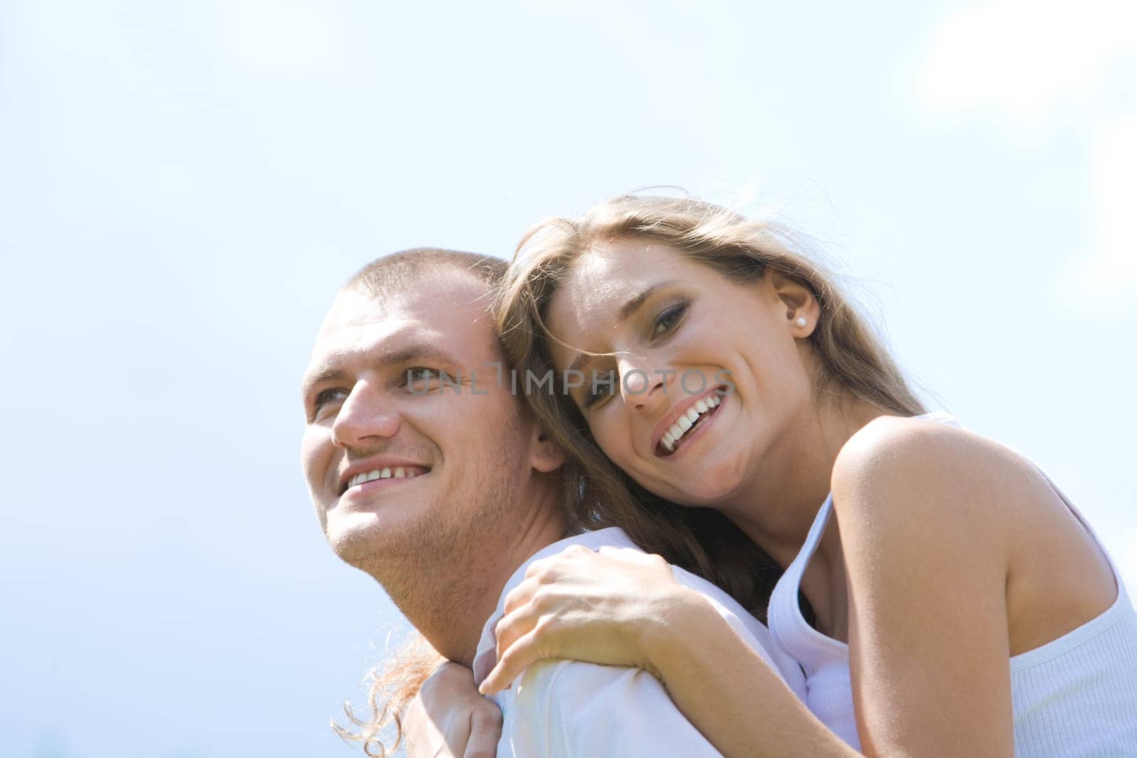 Laughing female embracing her husband on background of blue sky