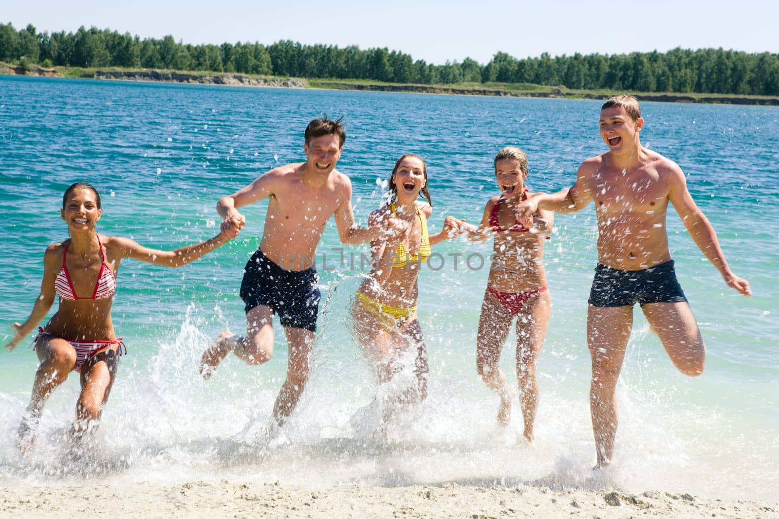 Portrait of young people running in water and laughing holding each other by hands