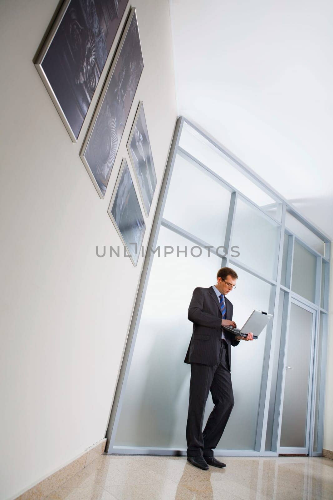Business man is standing in the corridor, holding the laptop