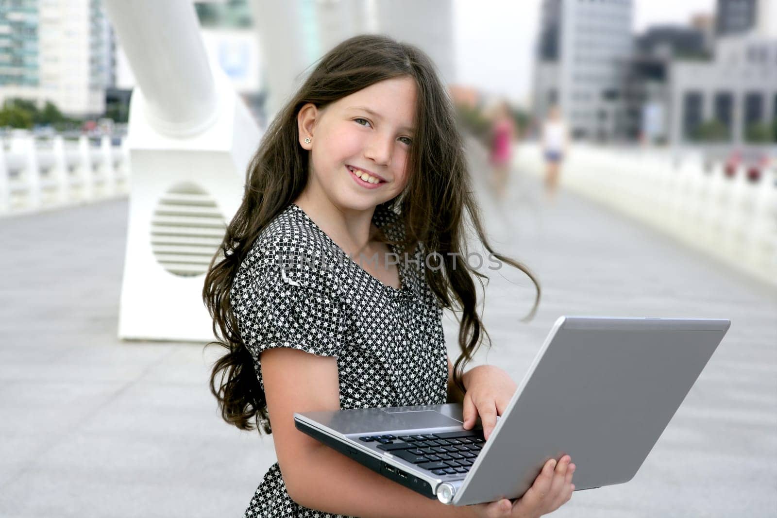 Beautiful little girl with laptop computer downtown city bridge