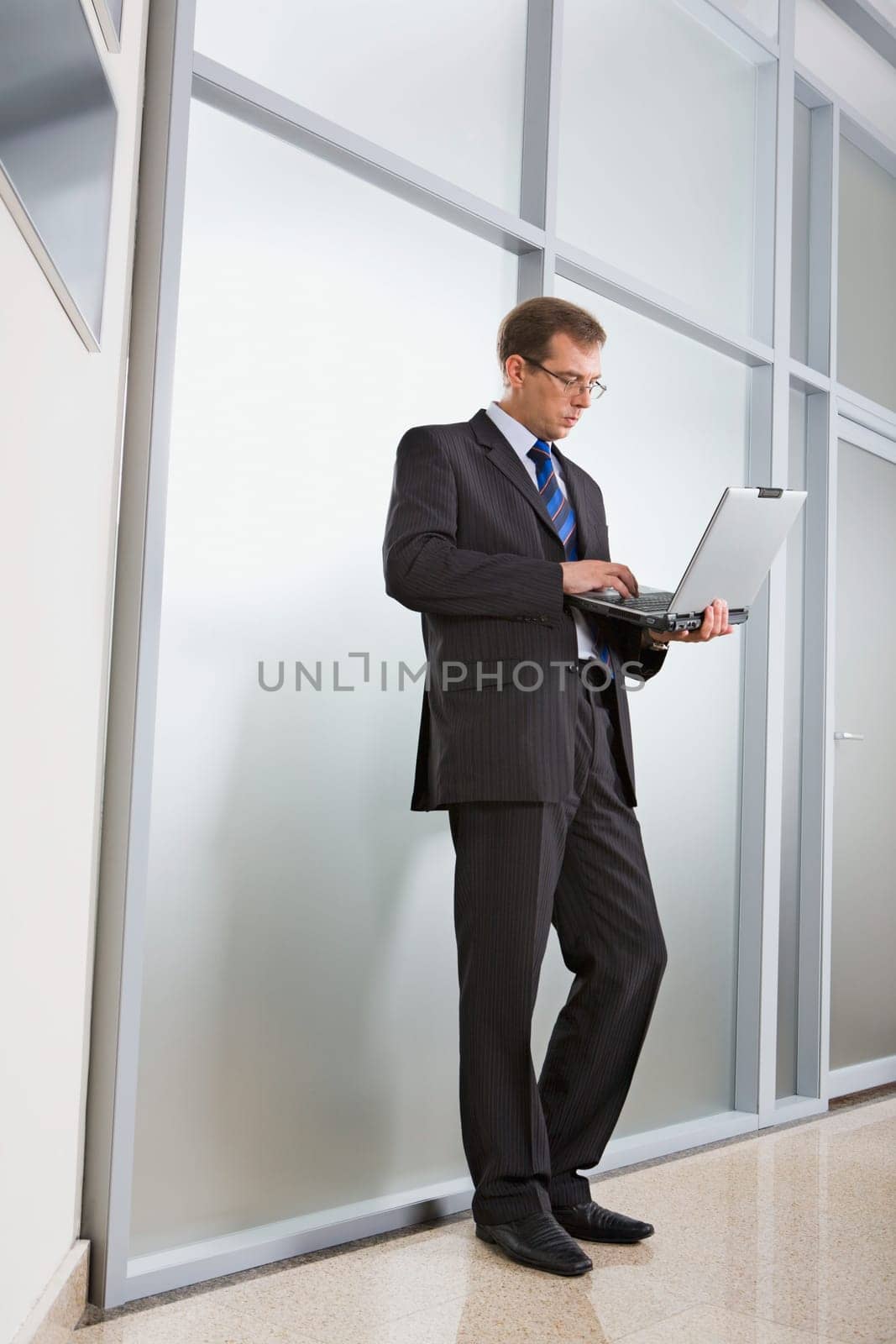 Portrait of thoughtful business man standing near the wall with laptop