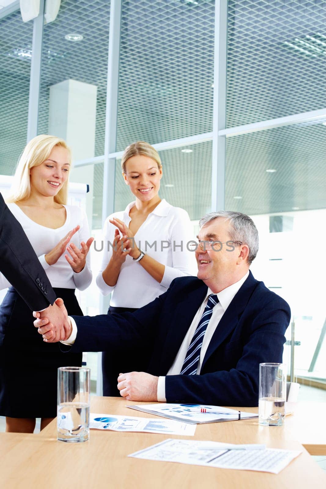 Senior chief shaking hands with his partner while two females on background clapping hands