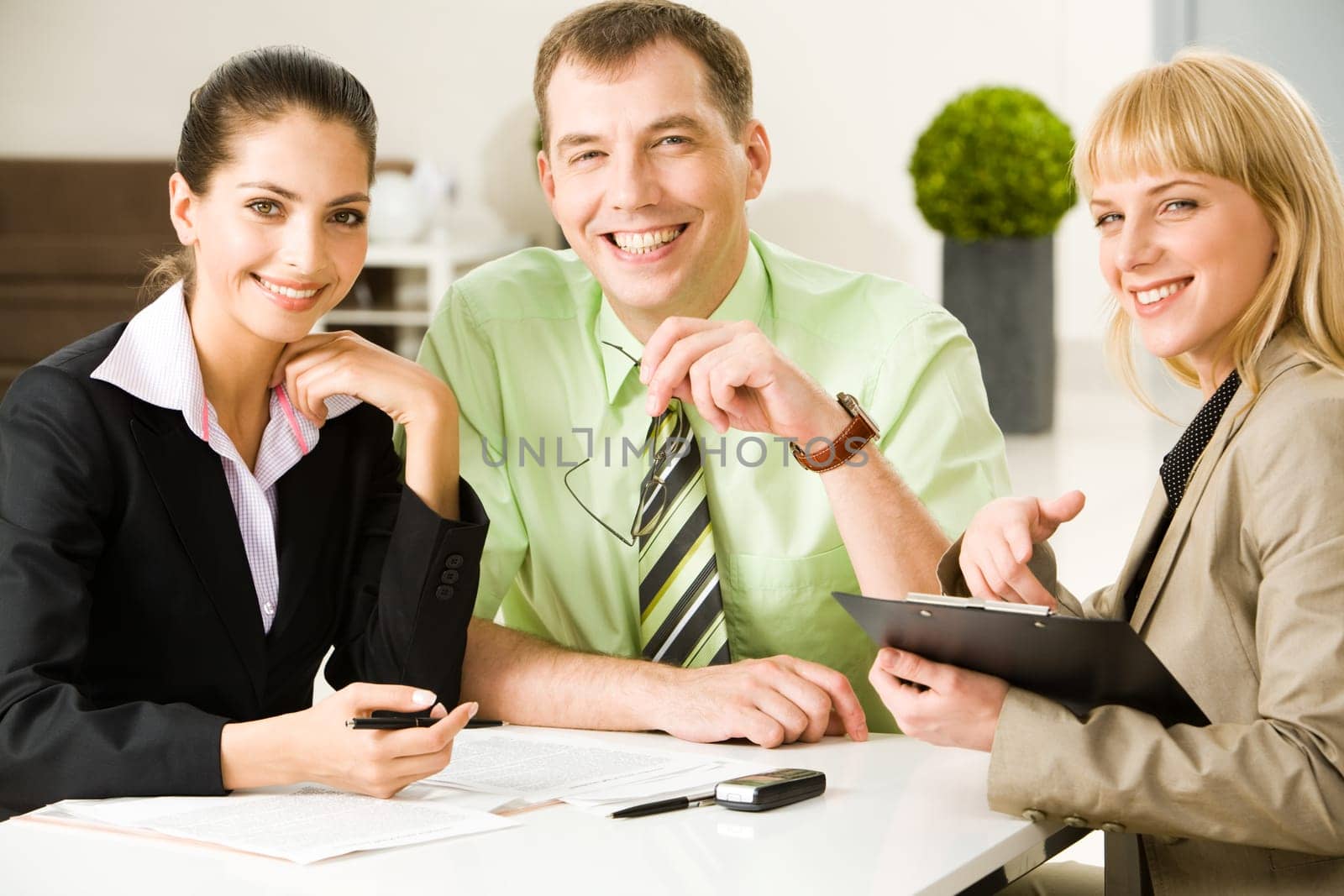 Photo of friendly business people sitting at table and looking at camera during working meeting