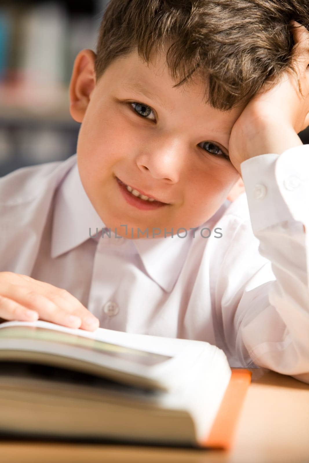 Close-up of smiling schoolkid touching page of open book and looking at camera with positive expression