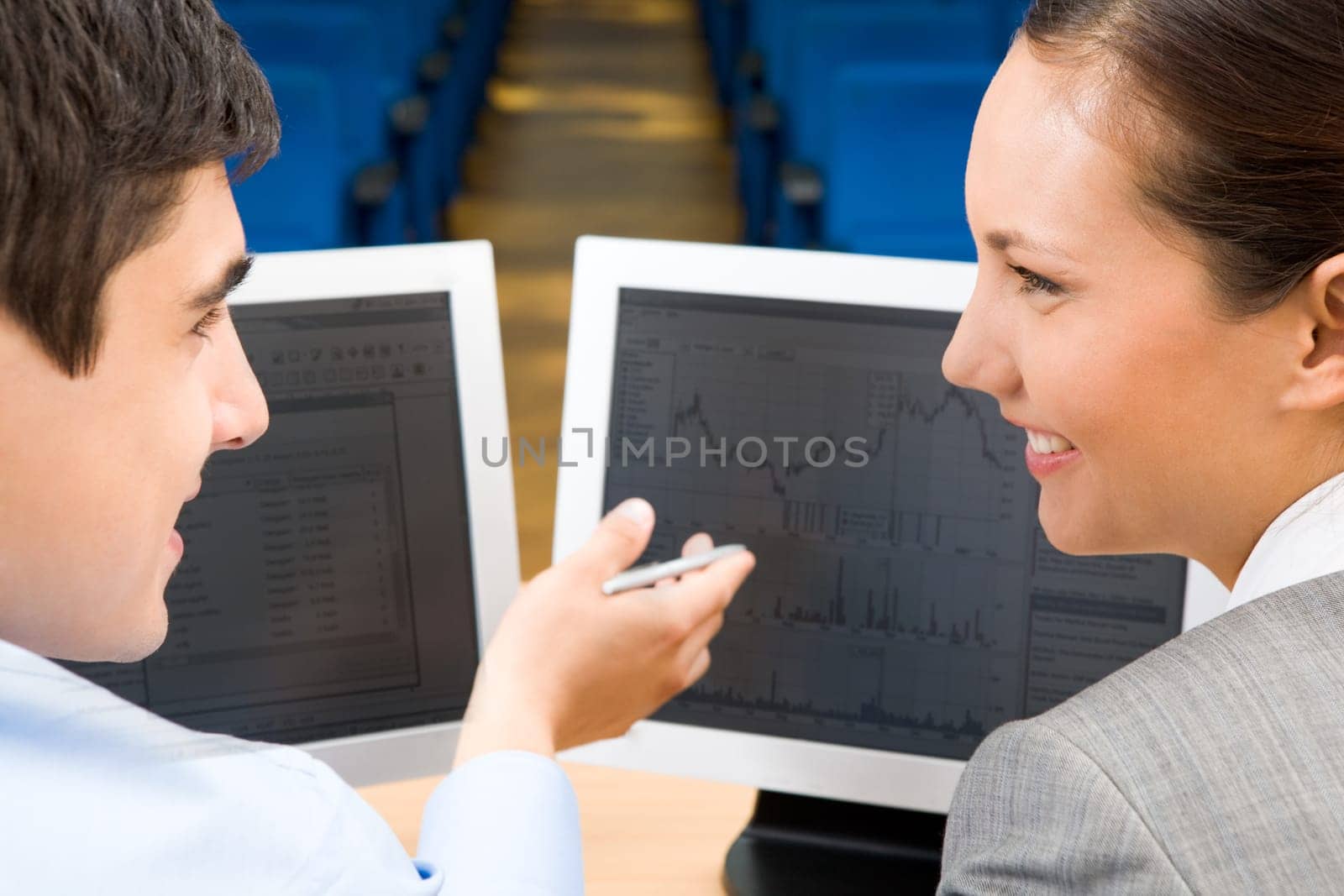 Successful businessman explaining something to his pretty colleague while they looking at each other in front of monitor