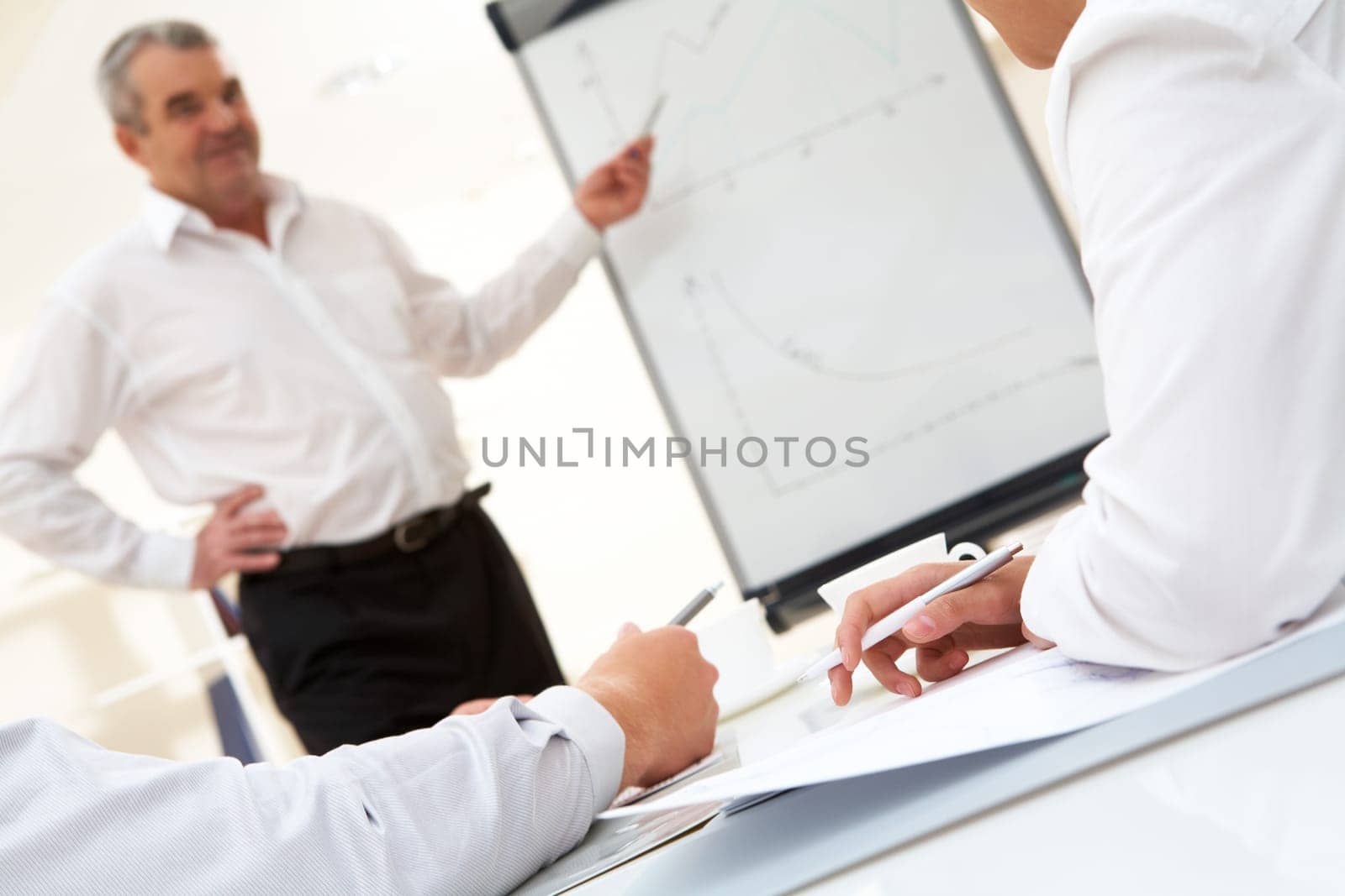 Photo of human hands over workplace on background of senior boss explaining his idea by the board