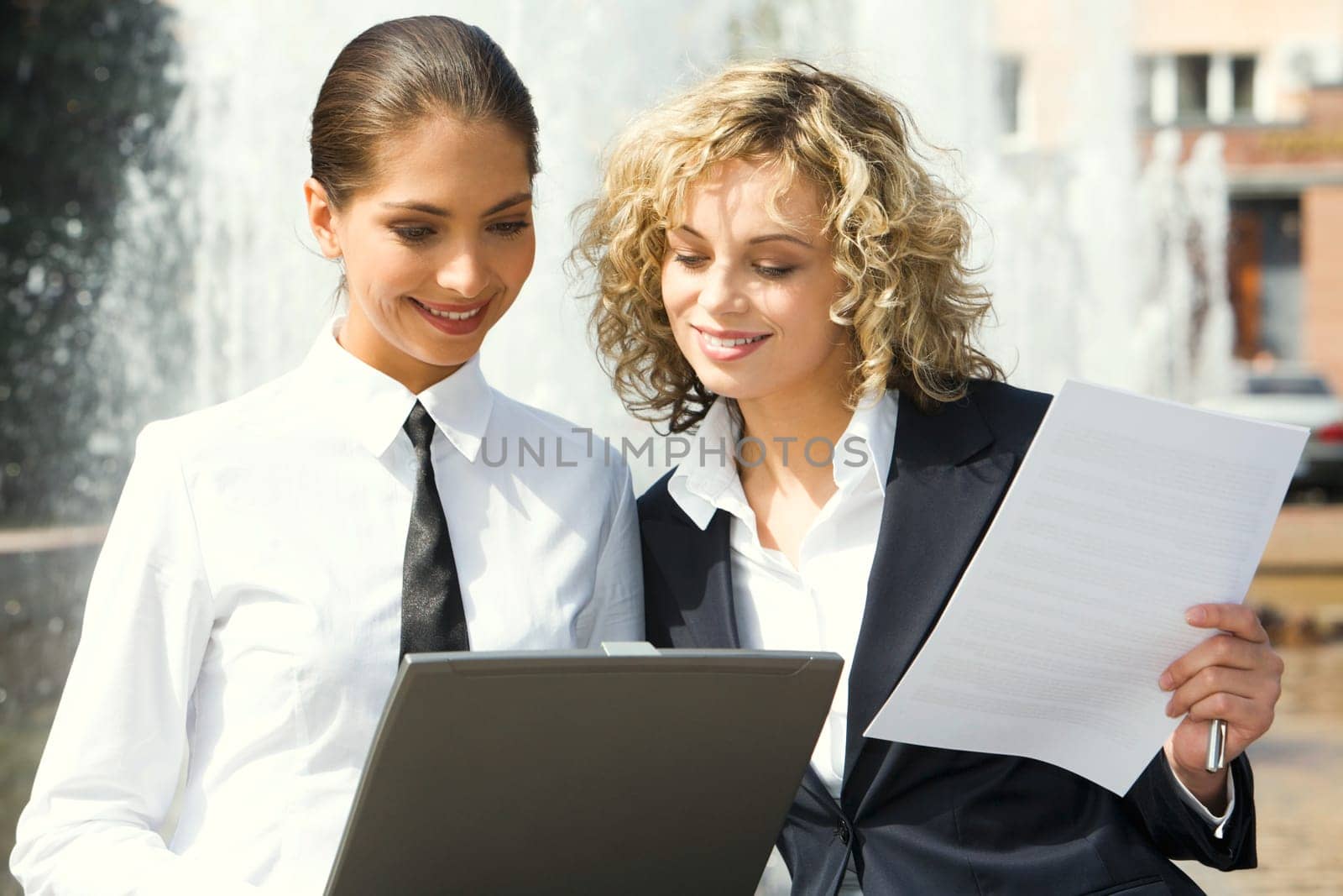 Cute smiling businesswomen reading documents outside and fountain on the background