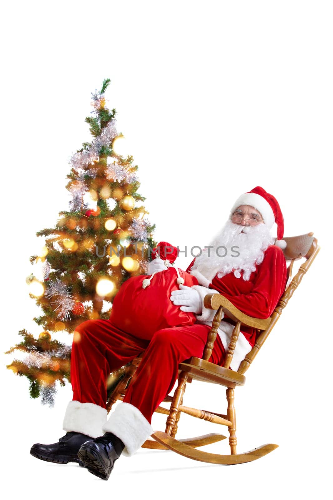 Santa sitting in the armchair at the Christmas tree and holding a sack isolated on white