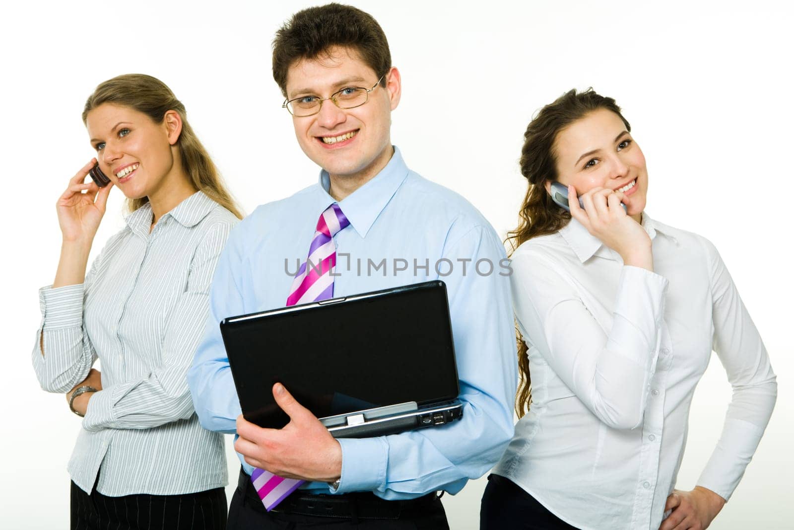 Photo of happy businessman with laptop standing between two smiling ladies speaking on cellphones