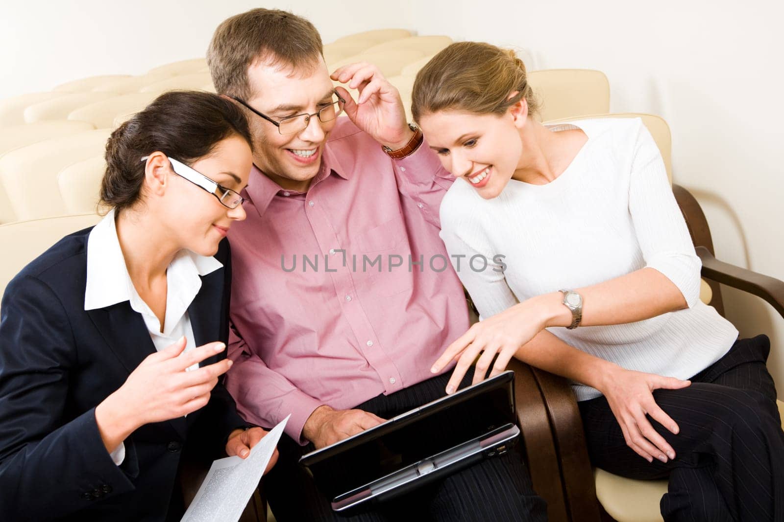 Image of three business people sitting in the armchairs and having a conversation during business meeting looking into the laptop screen