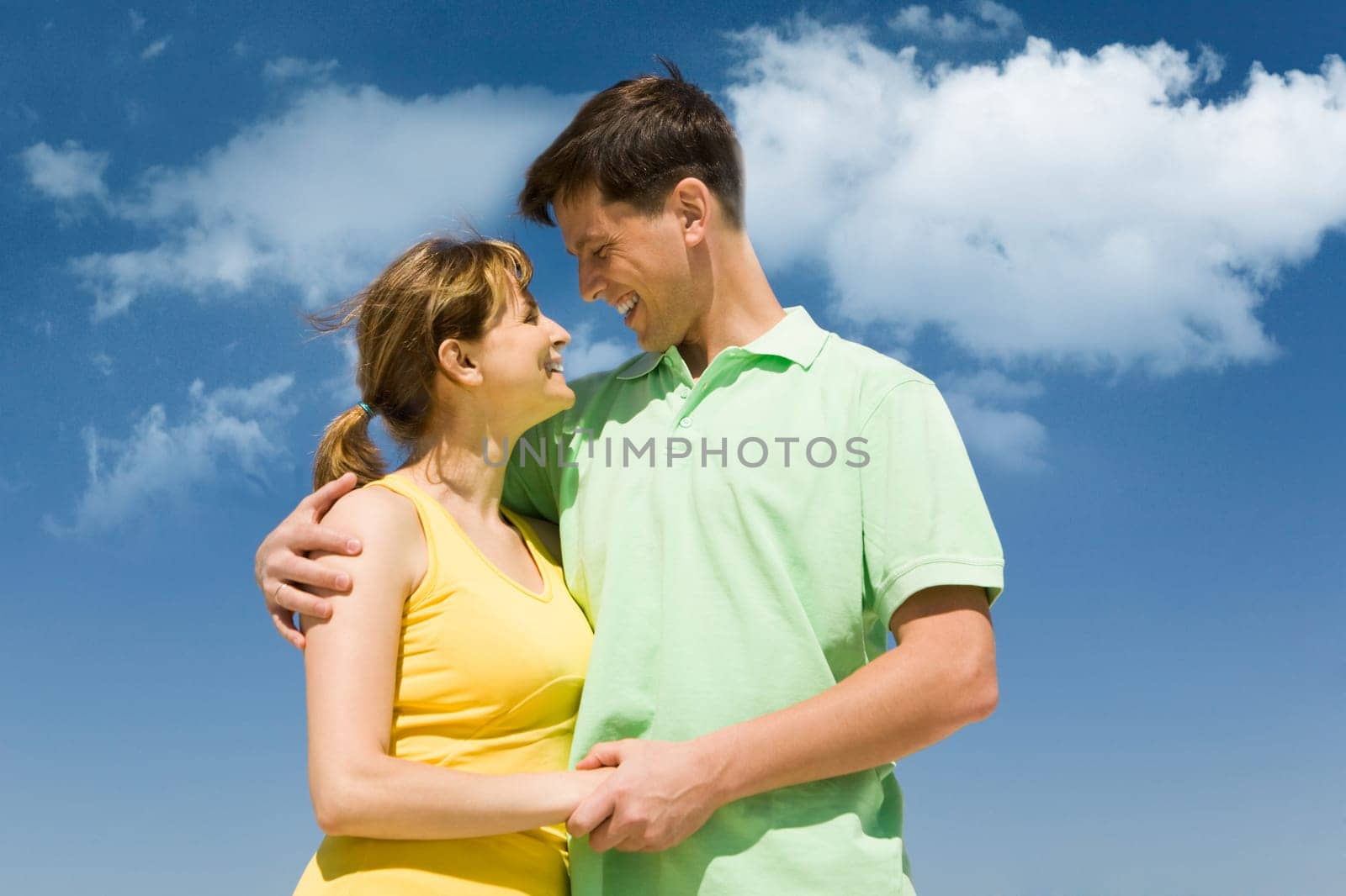Photo of amorous couple smiling at each other on background of bright sky