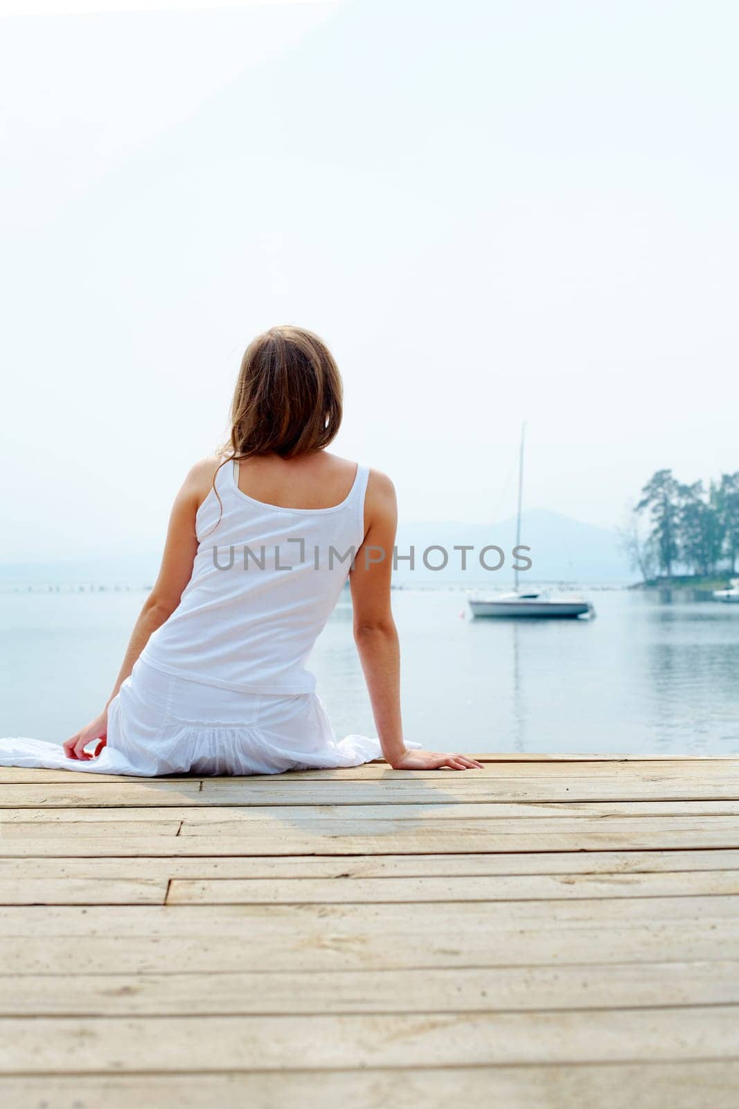 Rear view of pretty young lady in white cotton clothes having rest by the seaside