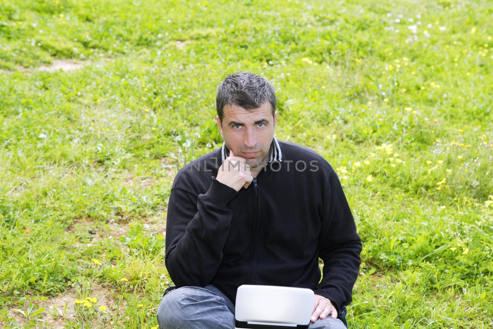 man working on meadow grass with notebook computer black winter sweater