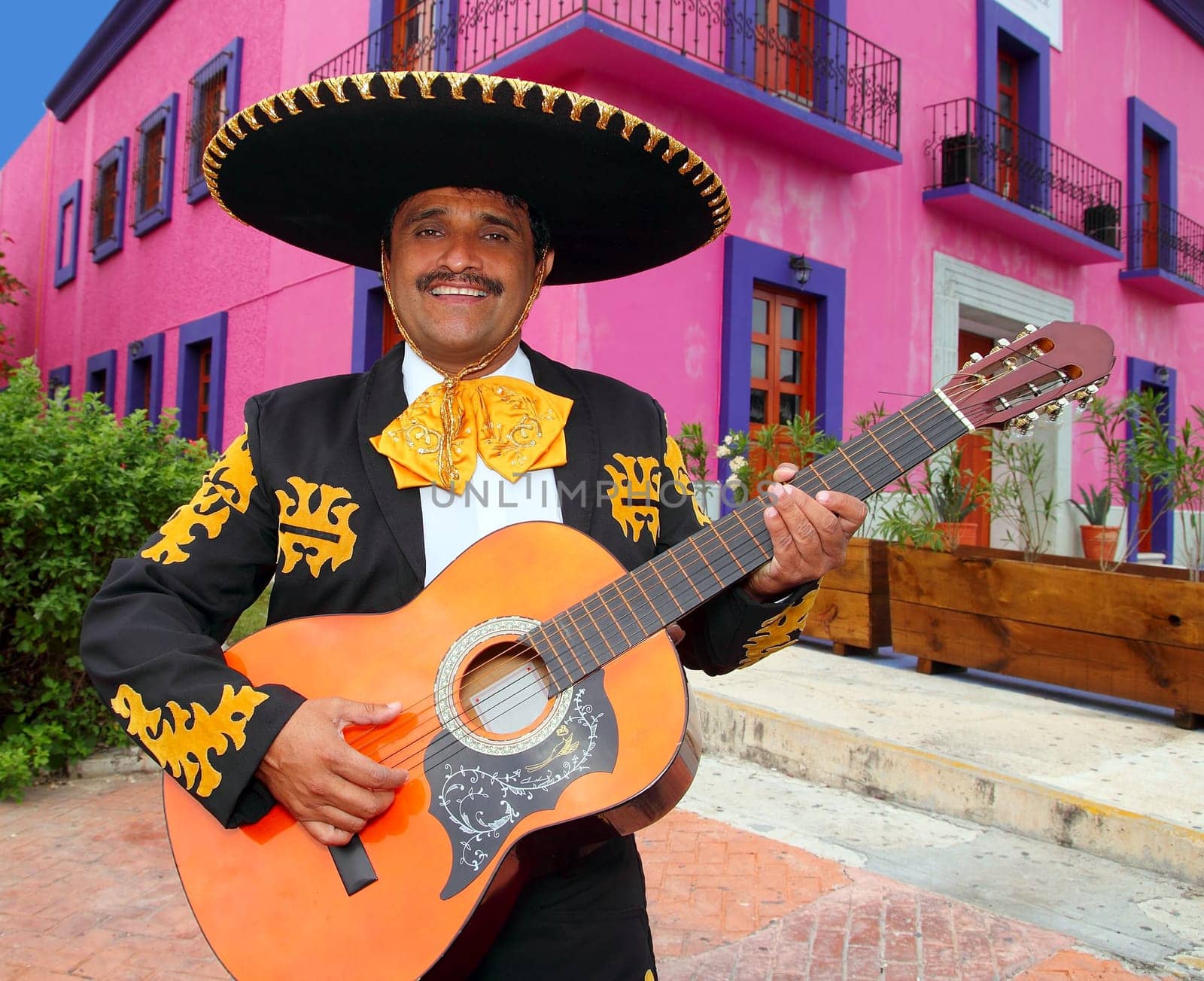 Charro Mariachi singer playing guitar in Mexico houses background