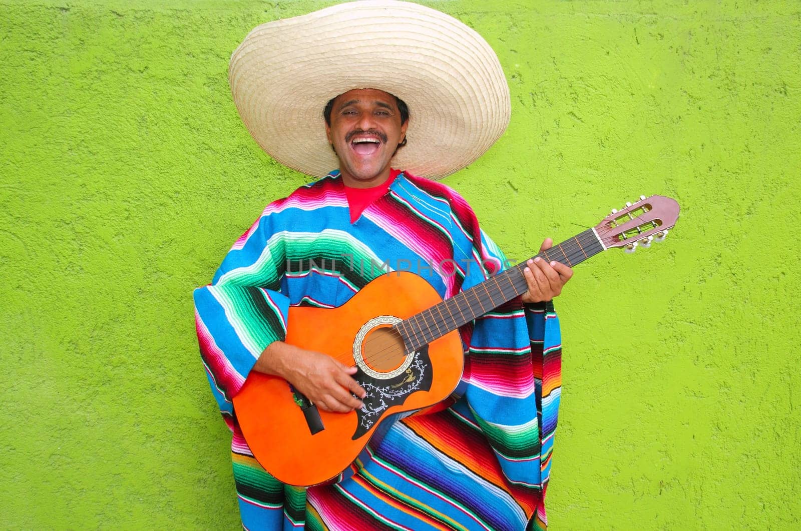 Mexican typical man playing guitar poncho on green wall