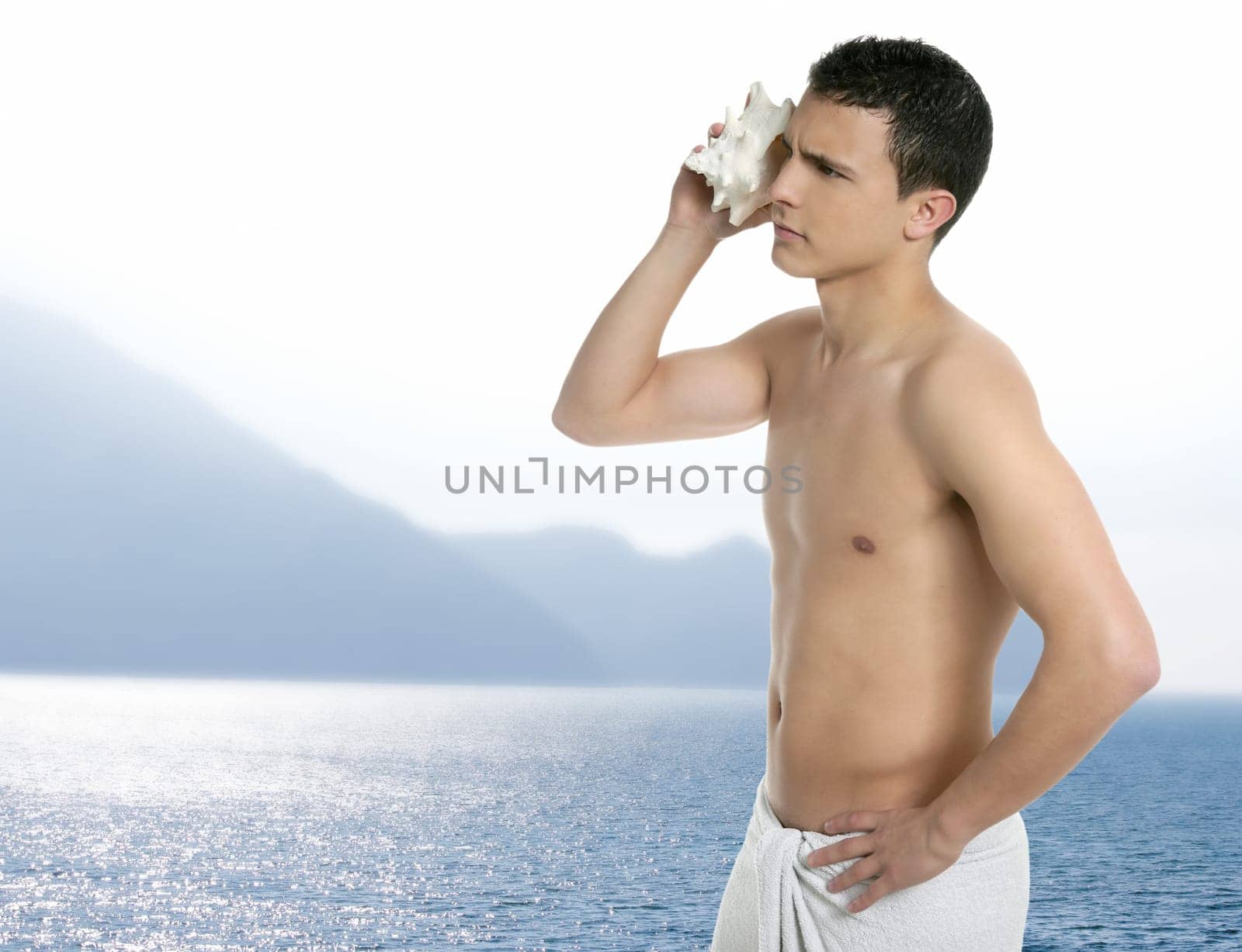Young handsome man after bath with towel, hearing waves on sea shell