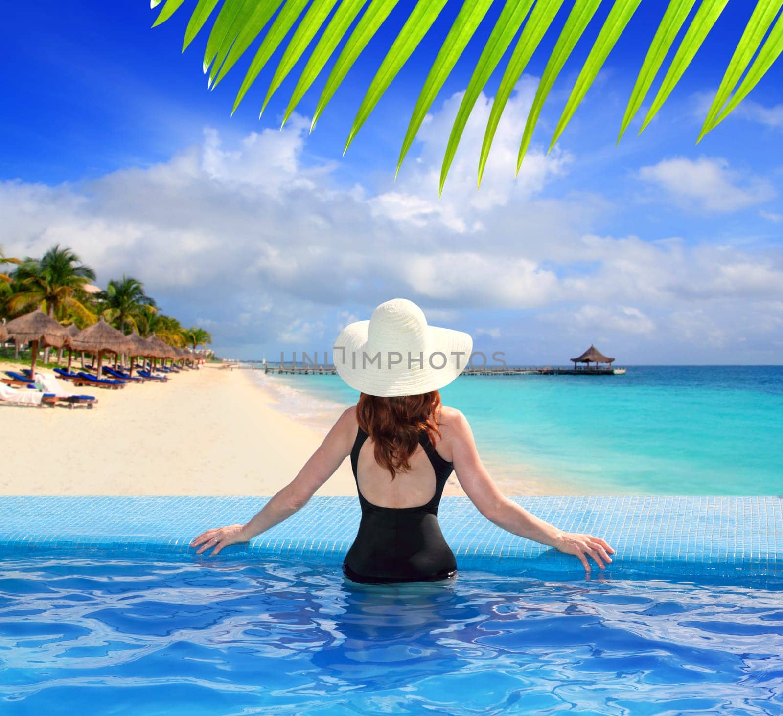 black swimsuit woman rear view in a pool with direct view to tropical Caribbean sea