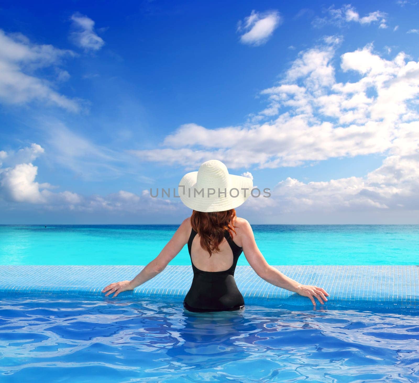 black swimsuit woman rear view in a pool with direct view to tropical Caribbean sea