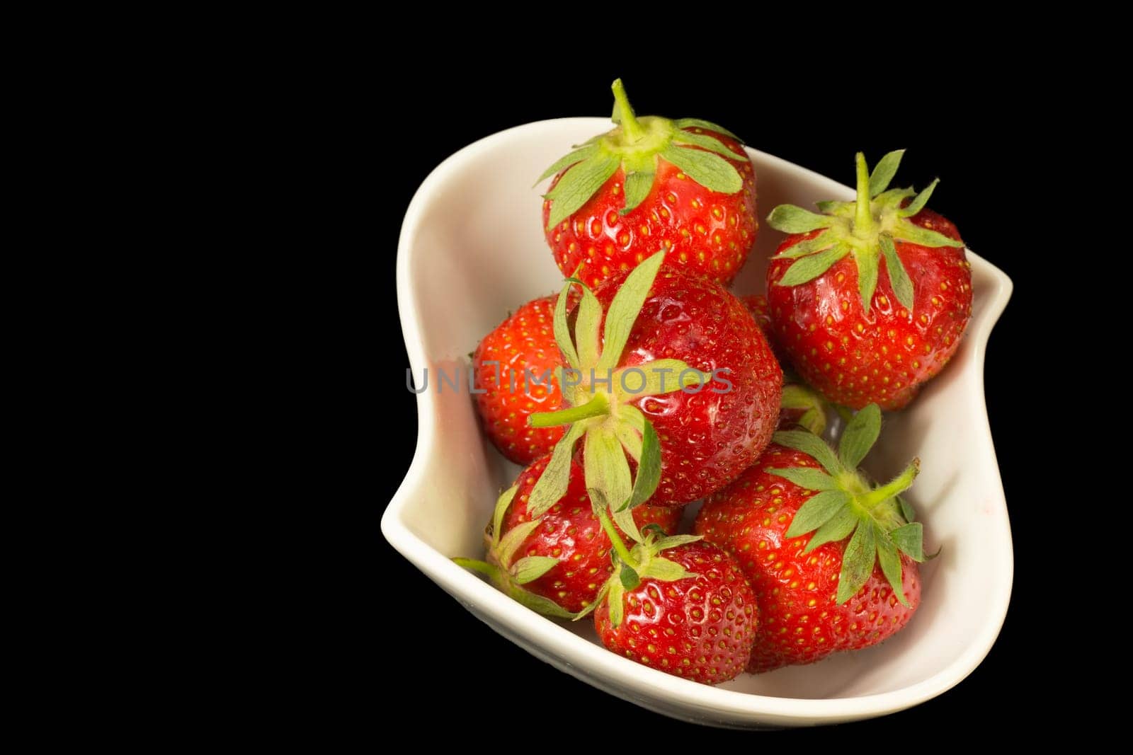 Fresh strawberries in white bowl on a black background. Horizontally.