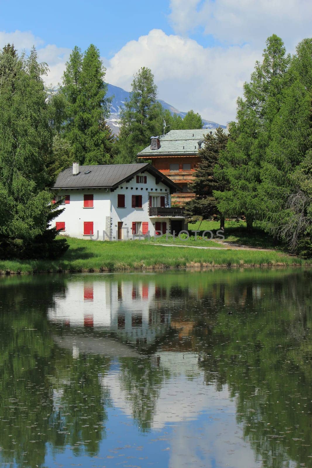 Two small house reflecting in the white lake by summer, Crans Montana, Switzerland