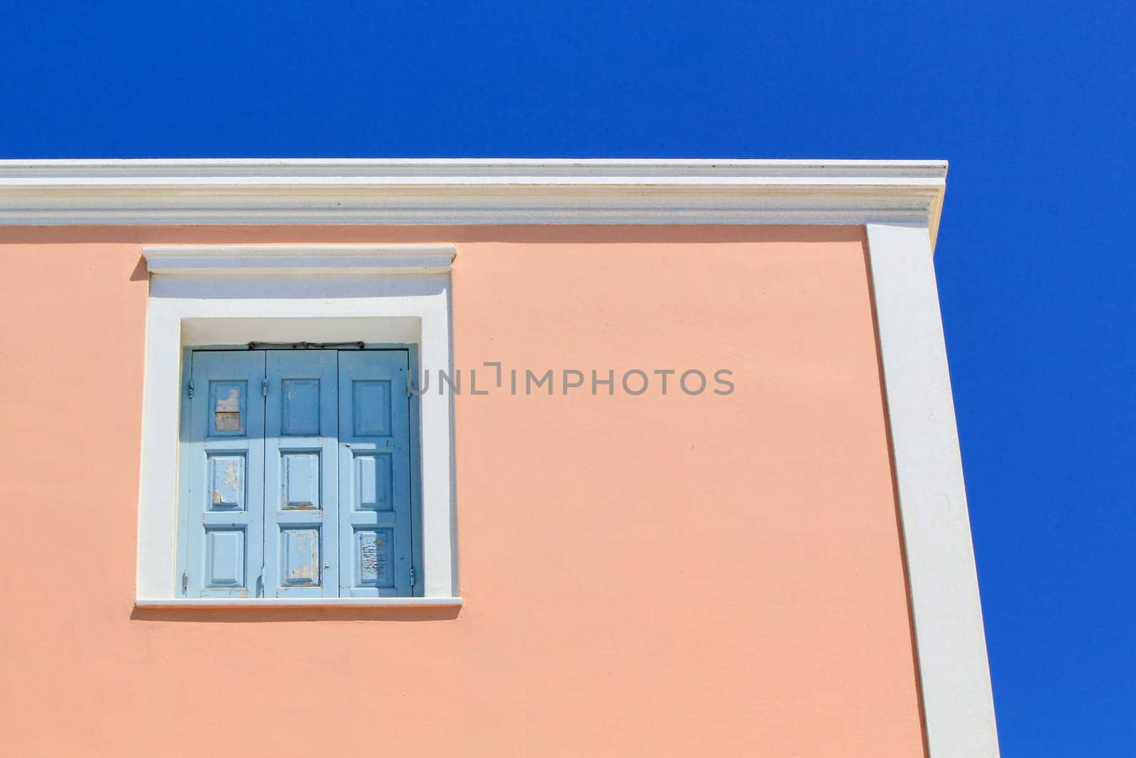 Colorful facade of a house with its blue closed shutters, red facade by beautiful weather, Santorini, Greece.