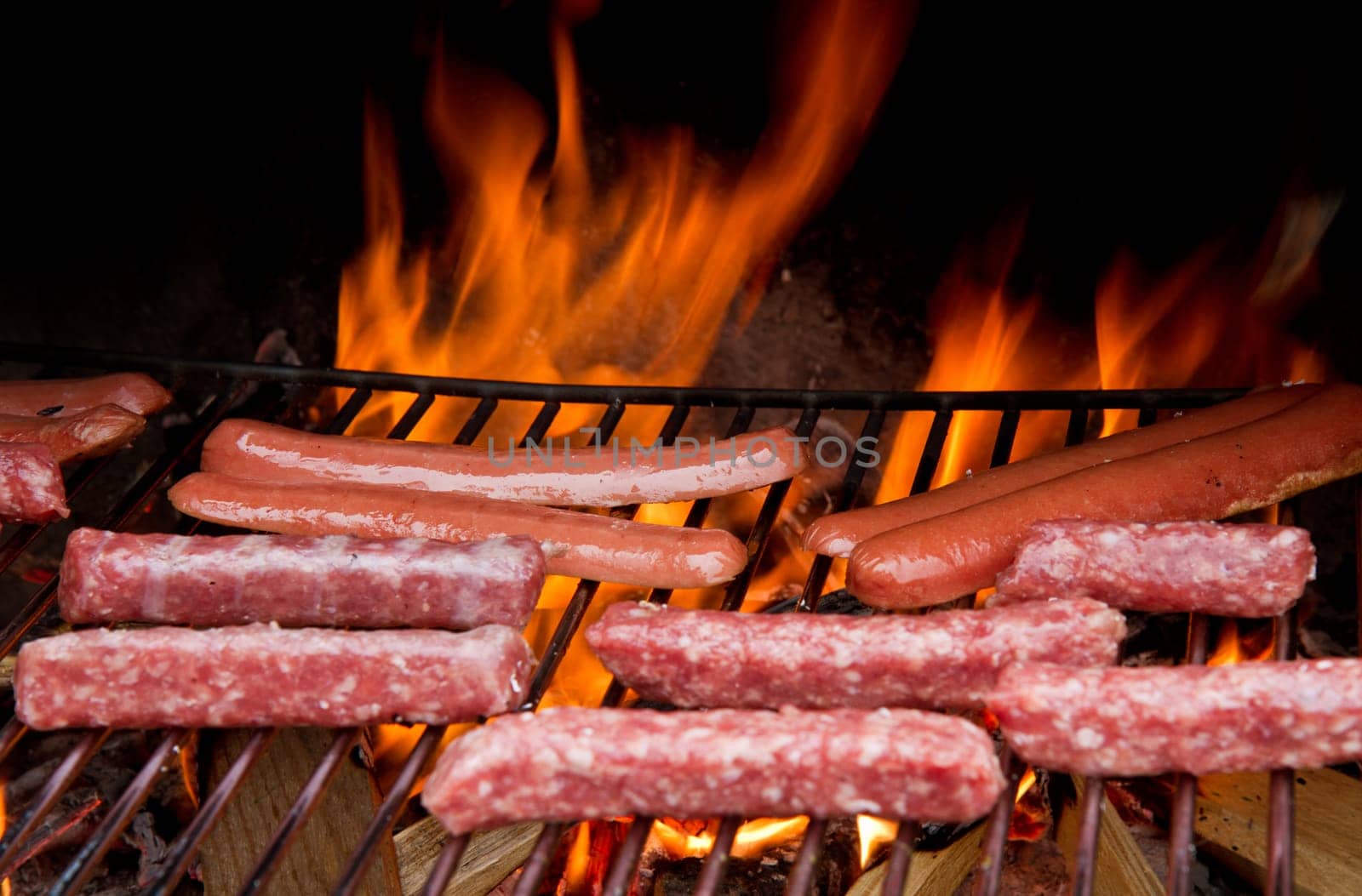 Brats  cooking on the grill with a flame in the background