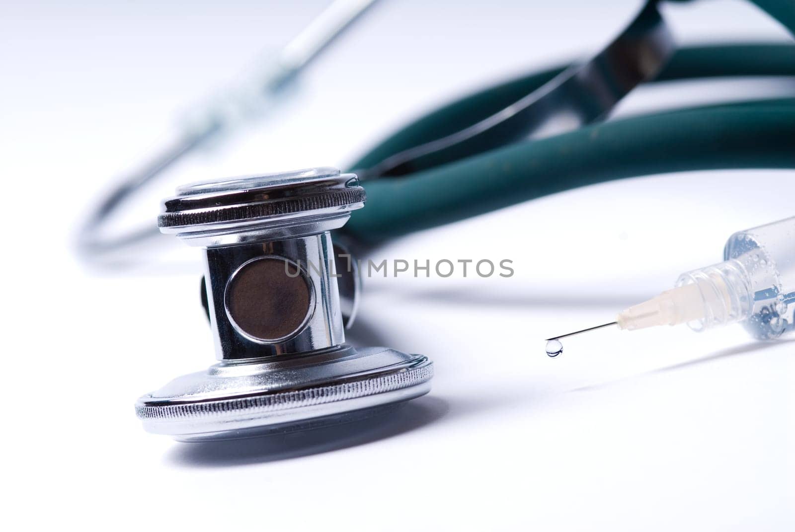 Stethoscope and a syringe in green on an isolated white background