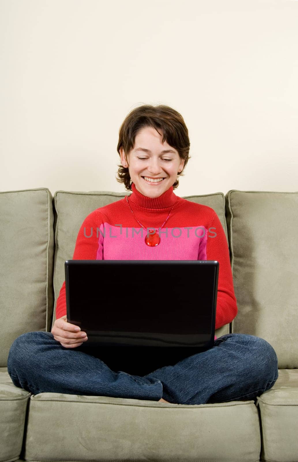 woman sitting cross-legged on green couch with laptop