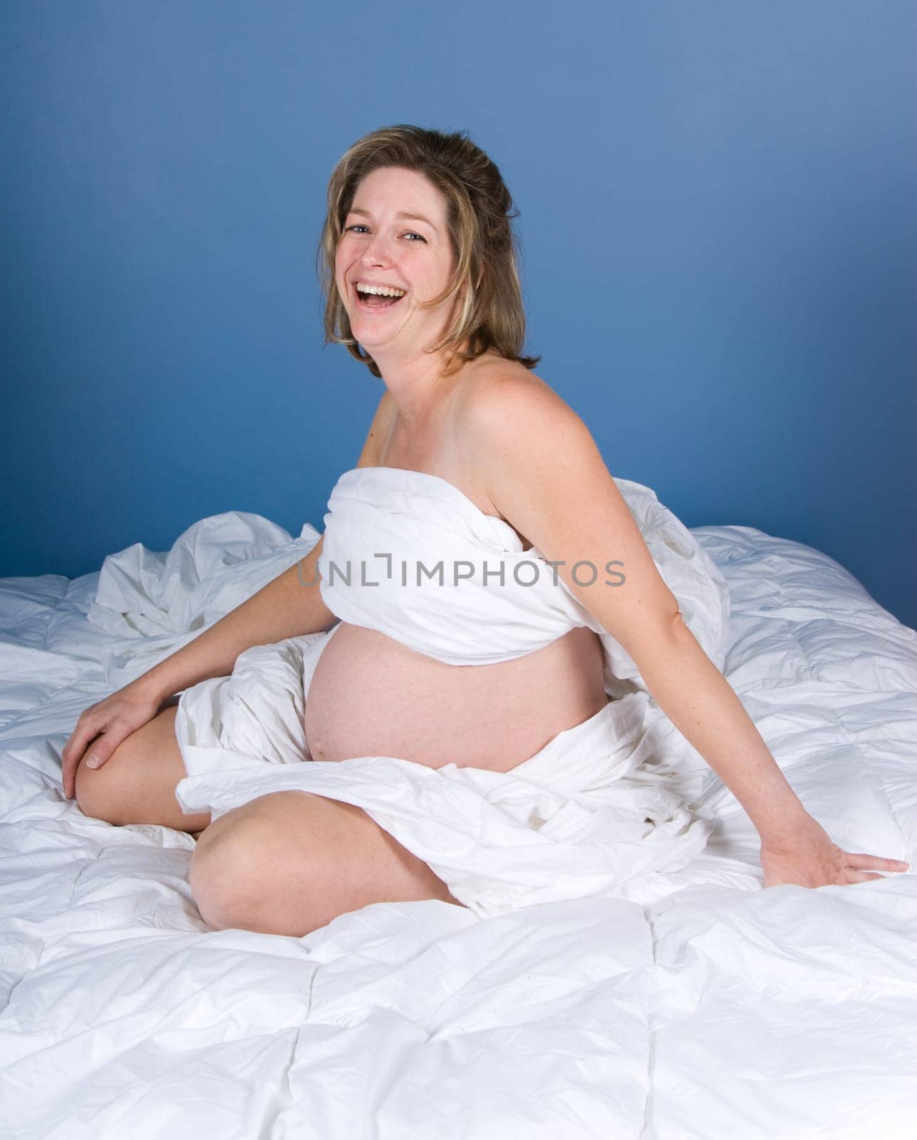 Happy pregnant woman on the bed with white sheets