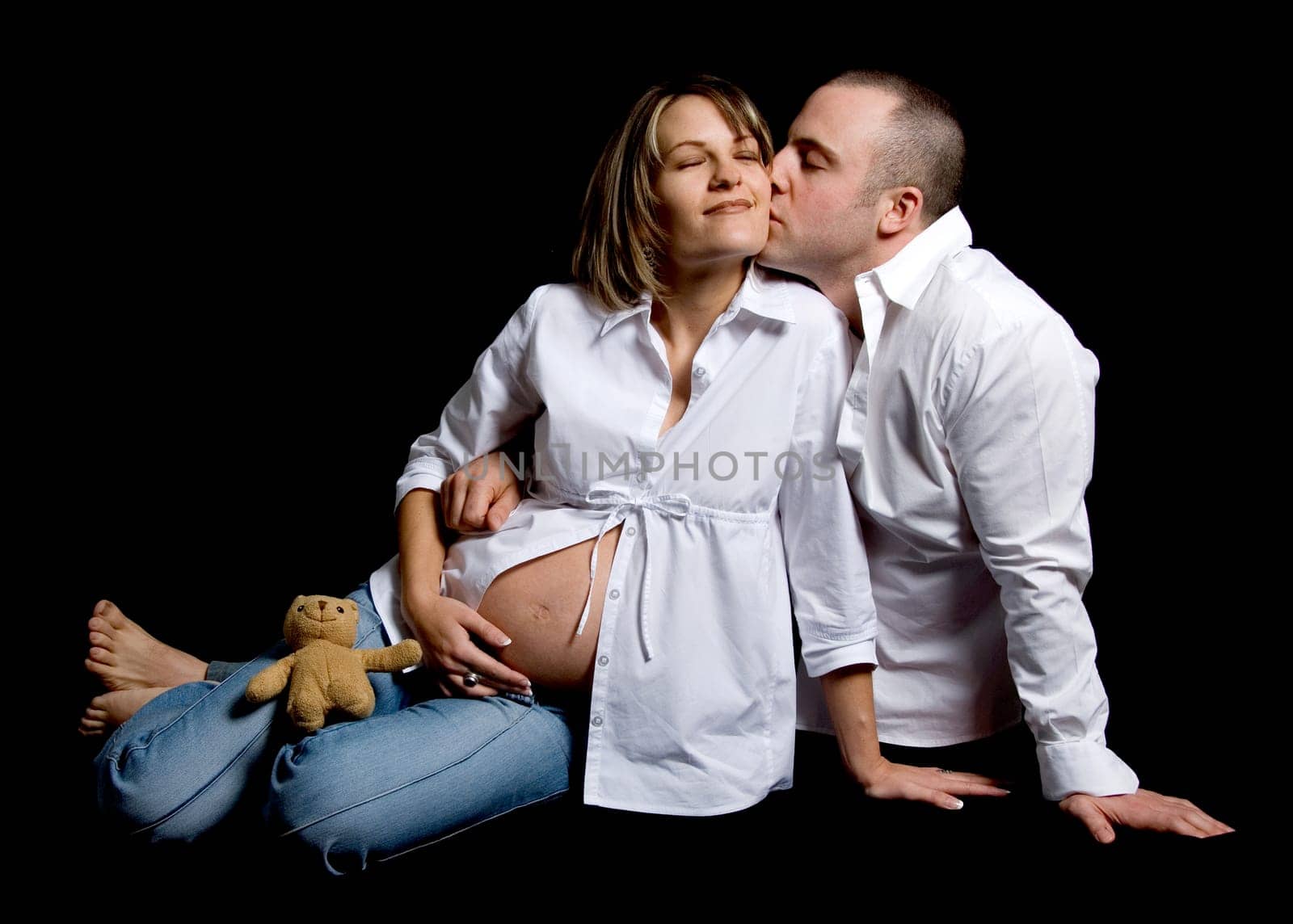 happy couple kissing with pregnant belly on black