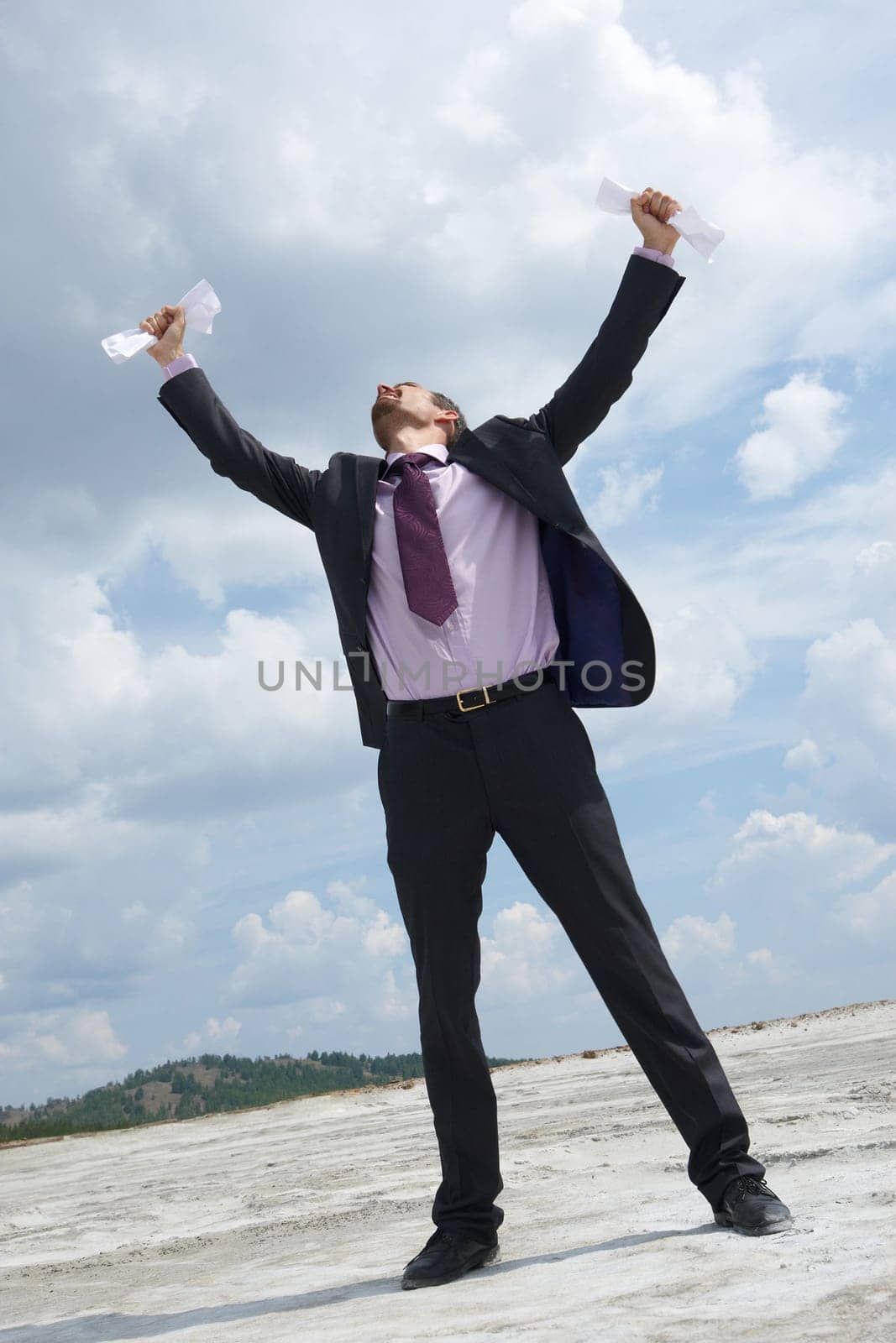 Photo of crying businessman standing and raising his arms with papers outdoors