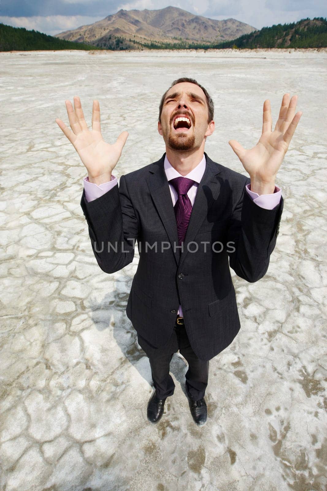 Photo of helpless businessman standing on dry ground and screaming with raised arms