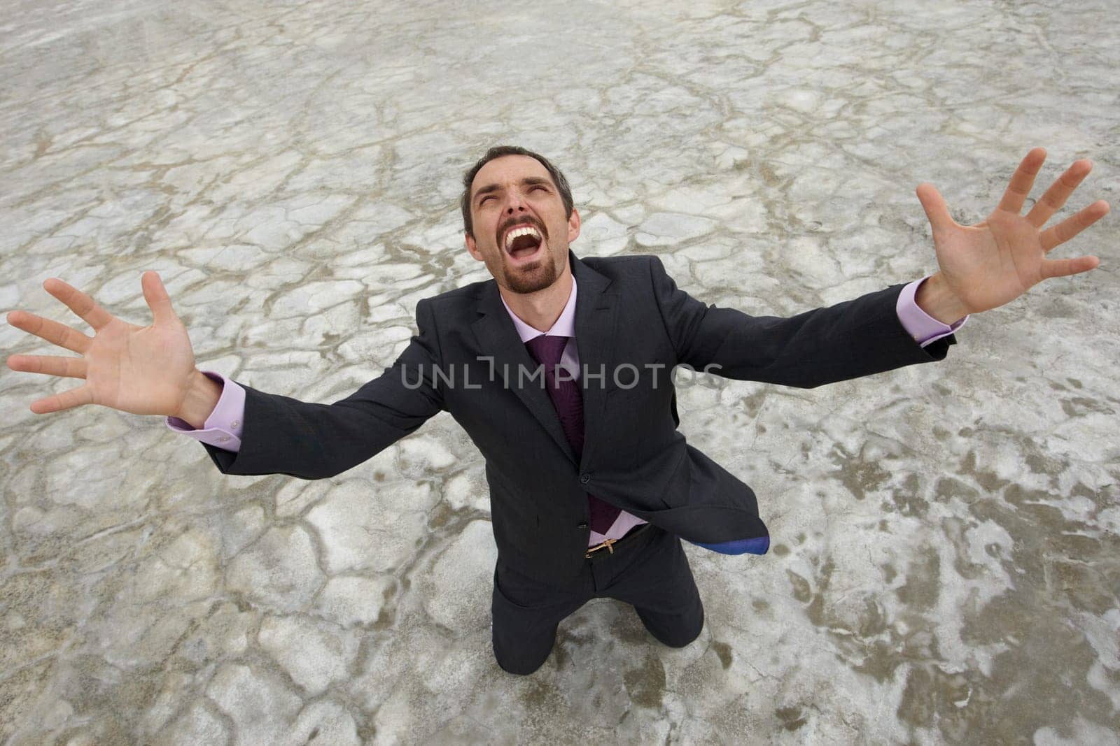 Photo of crying businessman standing on dry ground and raising his arms upwards