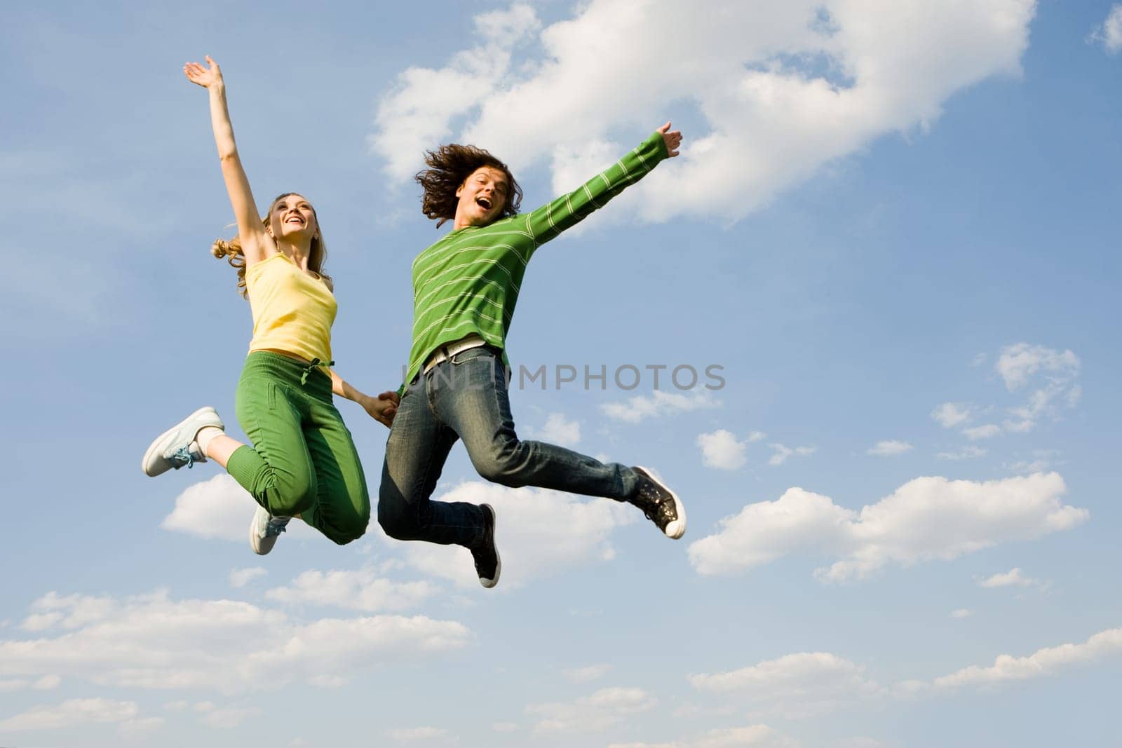 Image of cheerful girl and guy jumping high against bright blue sky and laughing