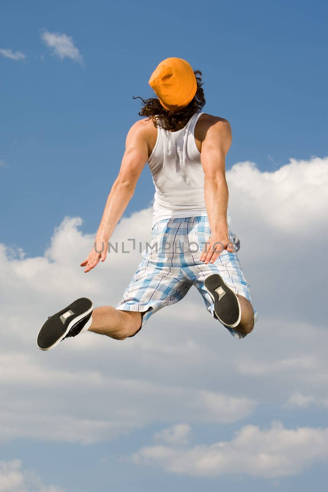 Rear view of energetic guy jumping high against bright blue sky