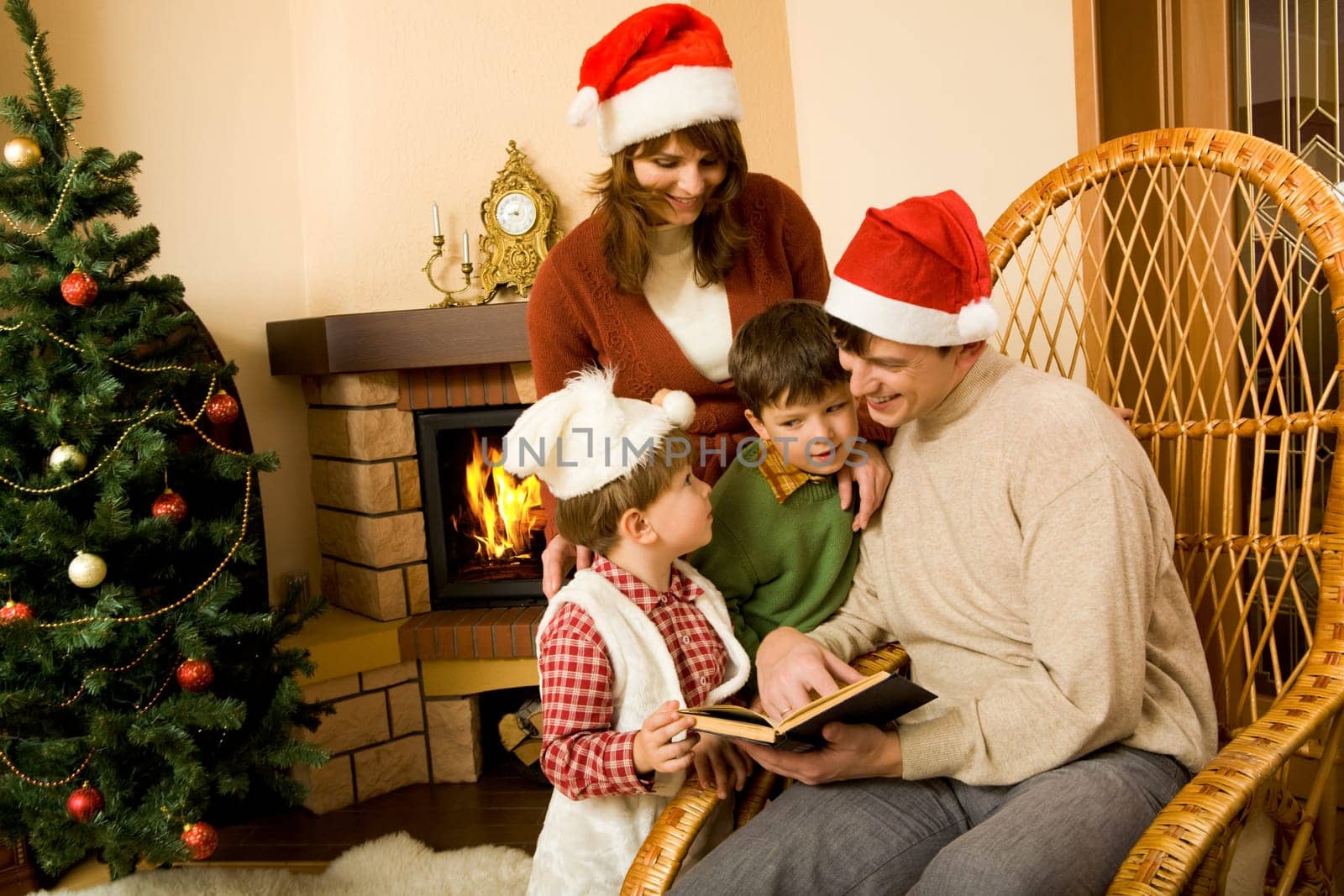 Portrait of smiling man with book in hand sitting in rocking-chair and looking at his little sons standing near by