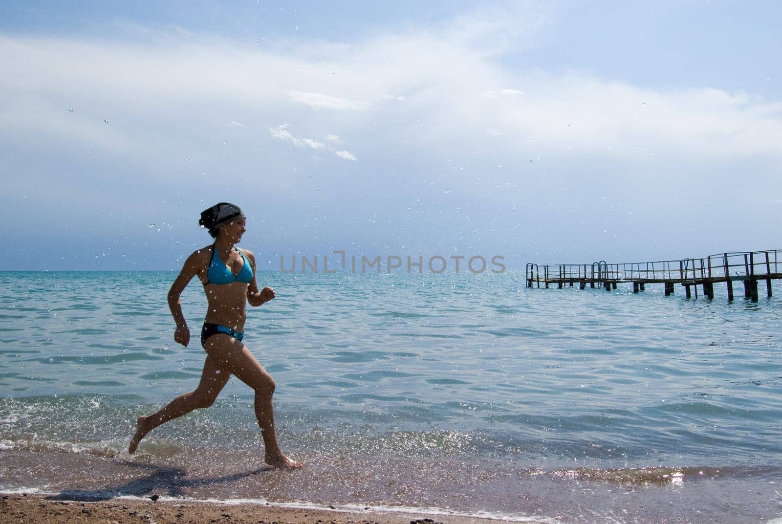 Photo of energetic female in swimsuit running along seashore during summer vacations
