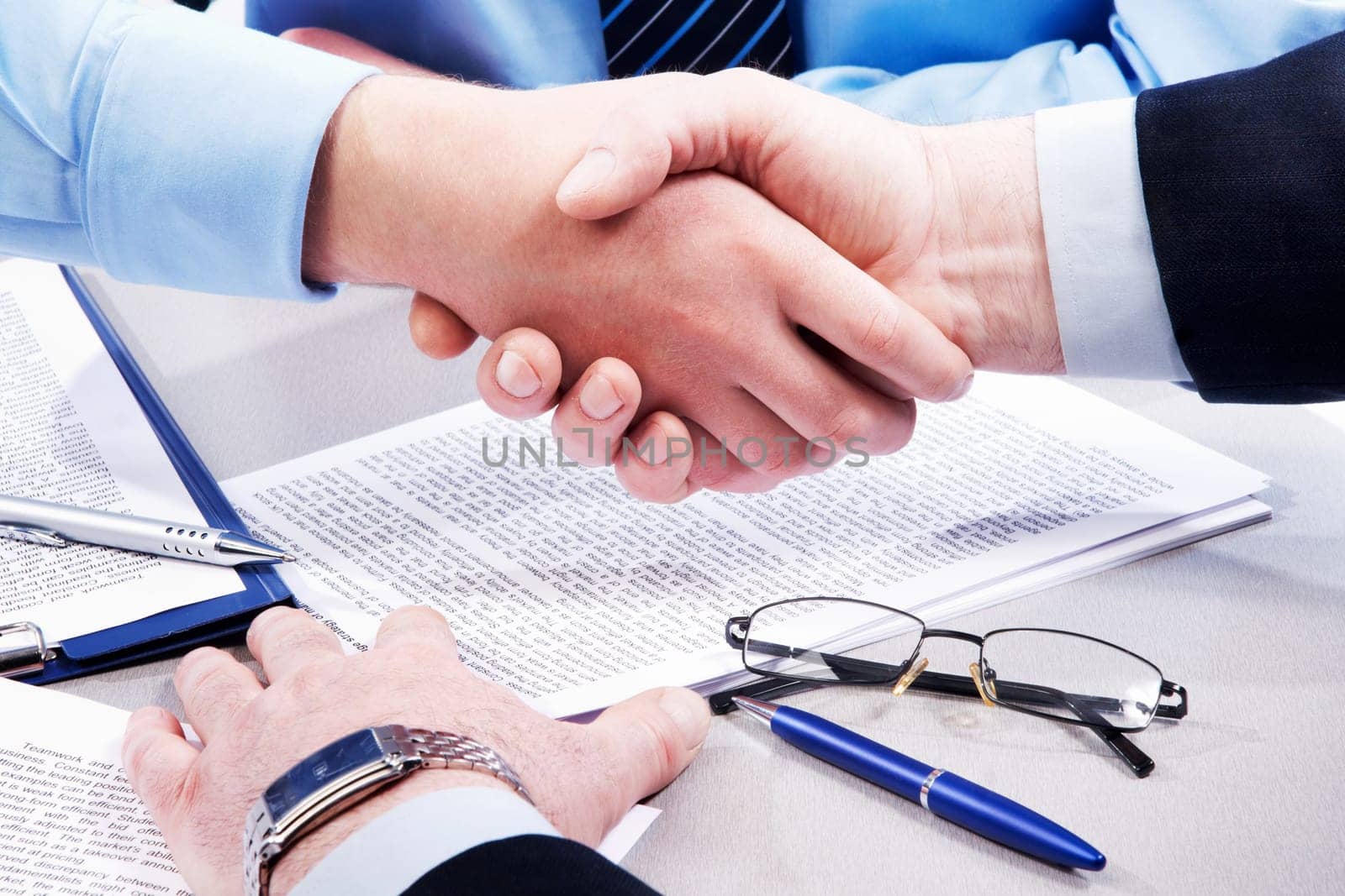 Close-up of business handshake over workplace with documents, pens, glasses