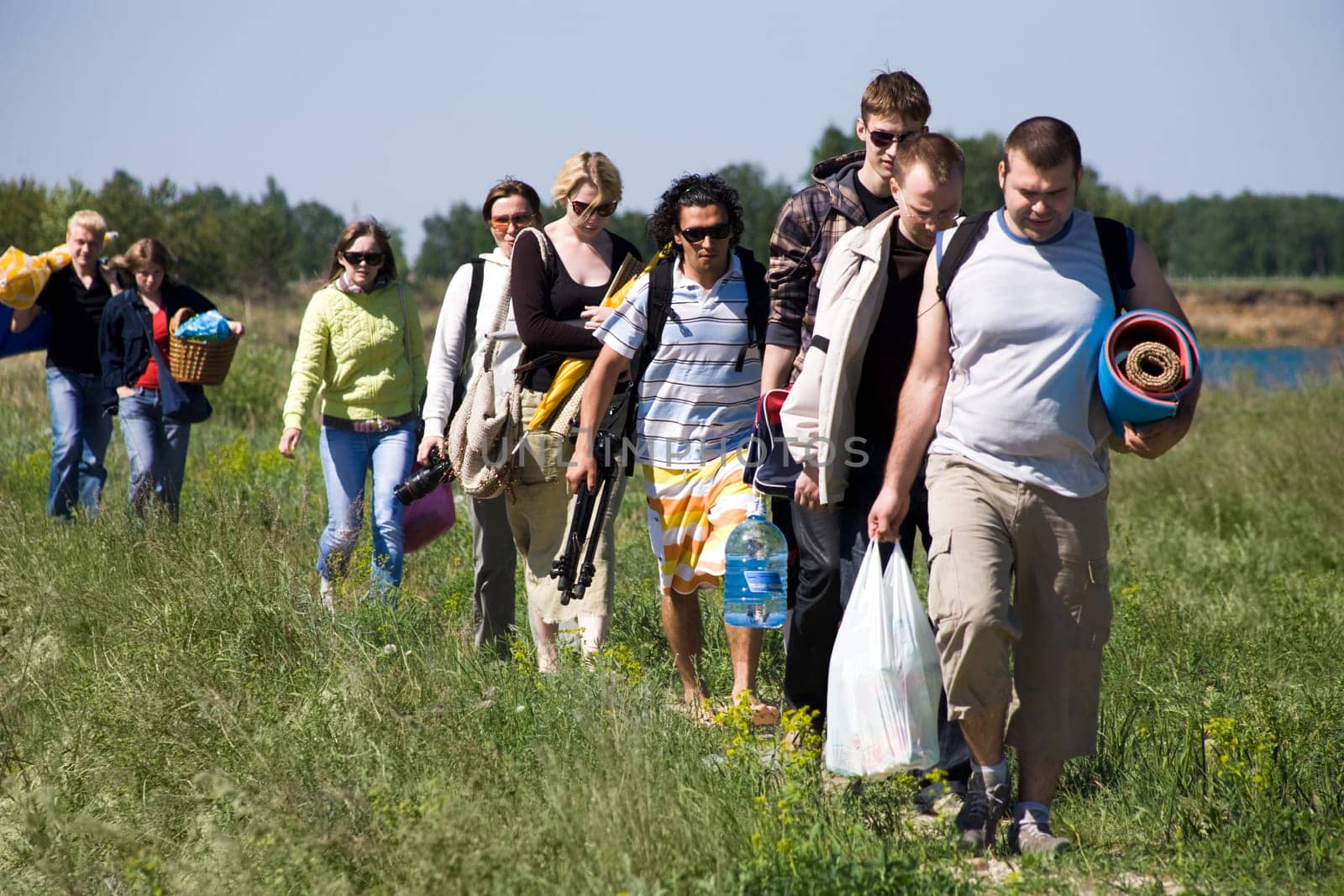 Image of queue of tourists walking down green grass while on trip outdoors