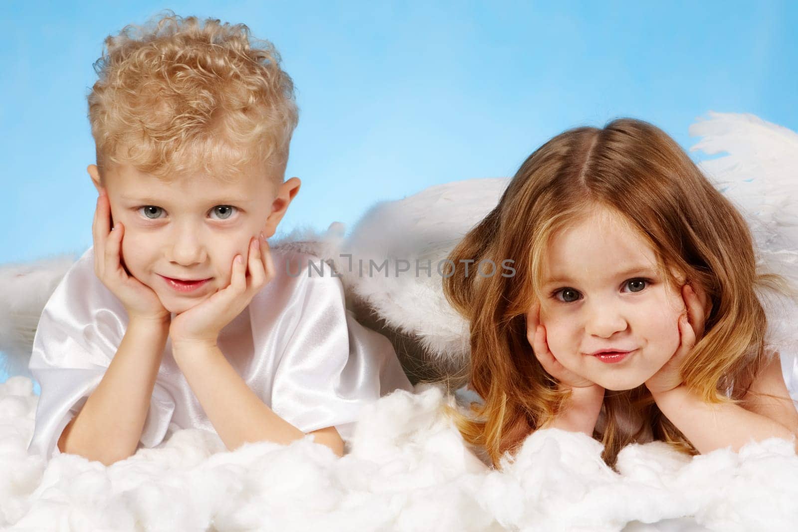Small boy and girl in angelic costume lying on white cloud