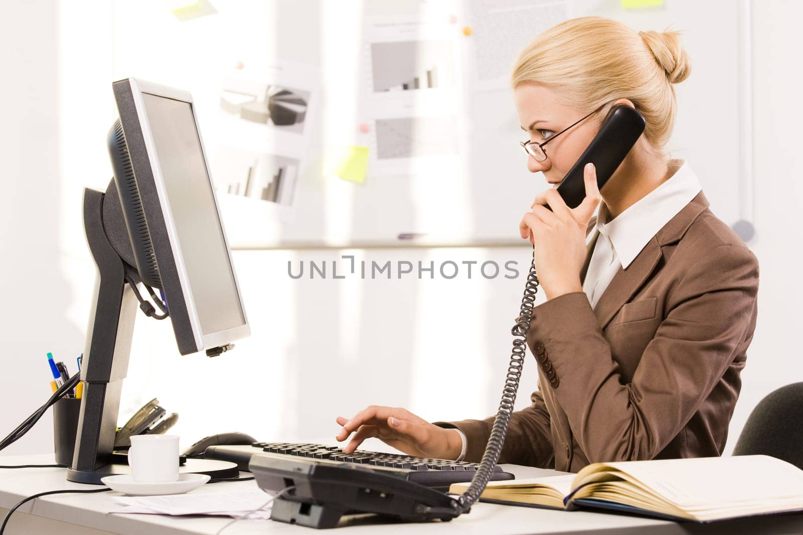 Busy secretary speaking on the phone while typing on keyboard and looking at computer screen