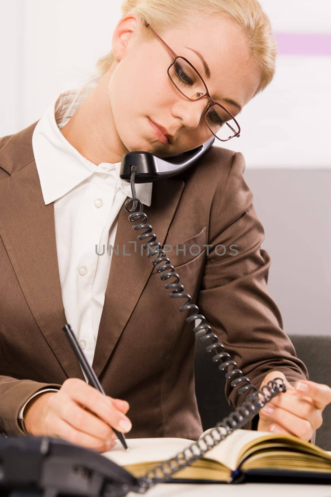 Photo of pretty clerk writing something down in notepad while speaking on the phone