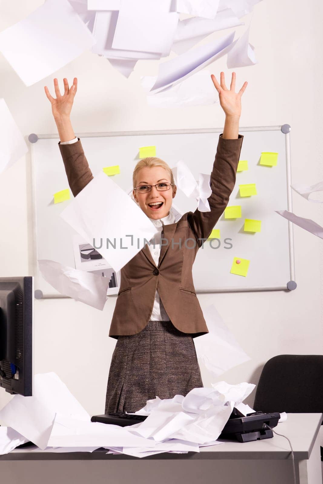 Portrait of happy businesswoman raising arms and throwing papers in office with laugh