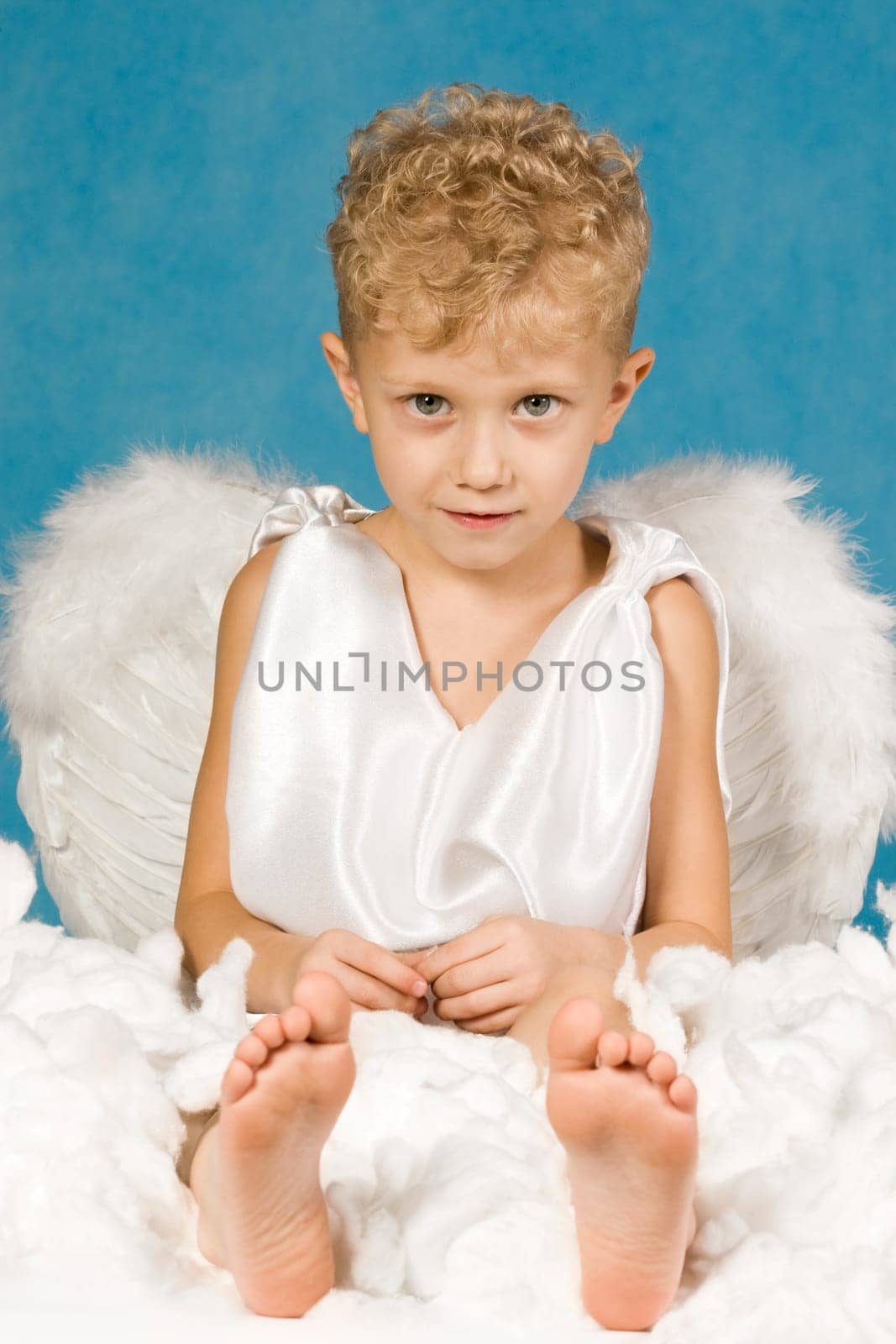 Portrait of cute boy in angel clothes sitting in cloud and looking at camera
