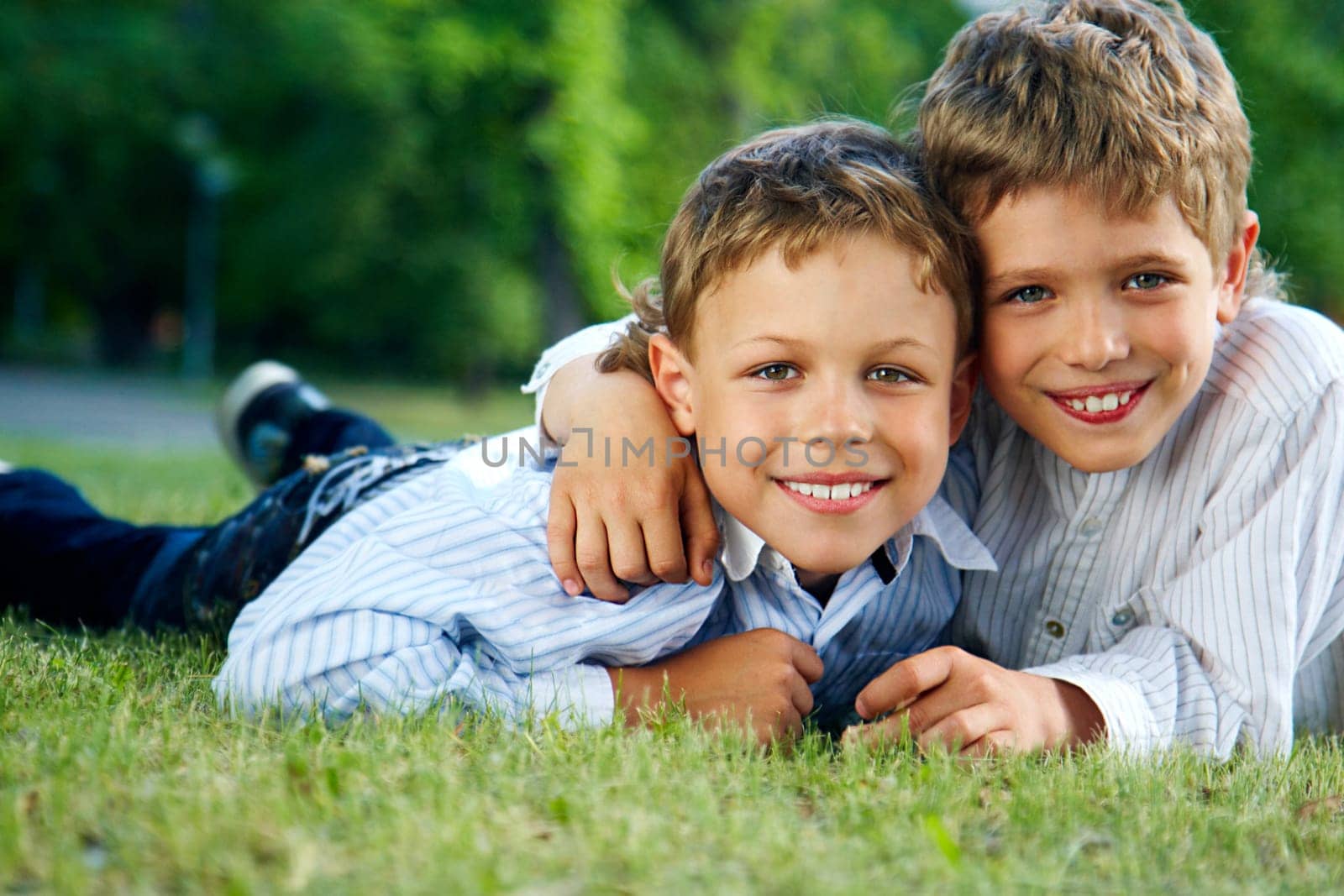 Portrait of happy boys lying on green grass and smiling at camera