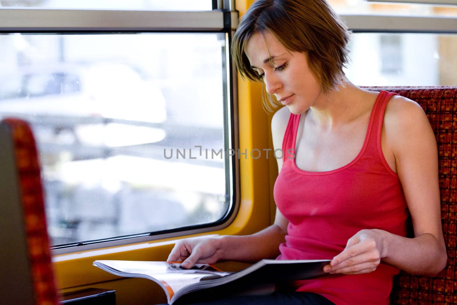 Photo of traveling passenger reading magazine in train by the window